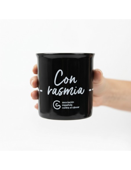 Taza solidaria negra con el lema Con Rasmia de la AECC sobre superficie neutra